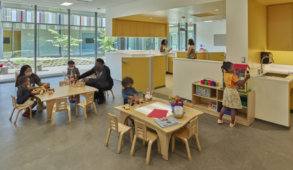 An early childhood education space with children engaged in activities and large windows providing natural light.