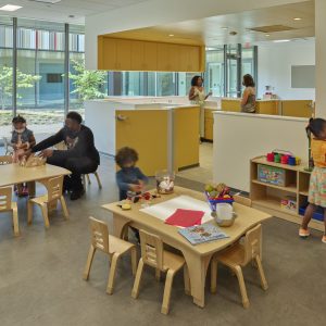 An early childhood education space with children engaged in activities and large windows providing natural light.