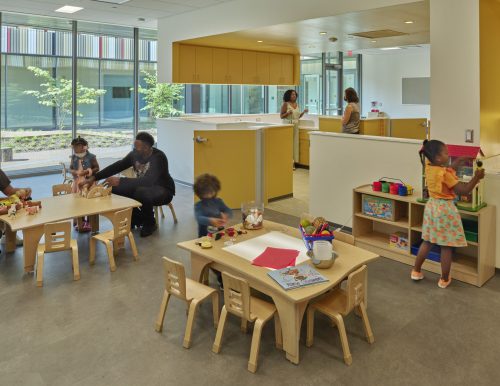 An early childhood education space with children engaged in activities and large windows providing natural light.
