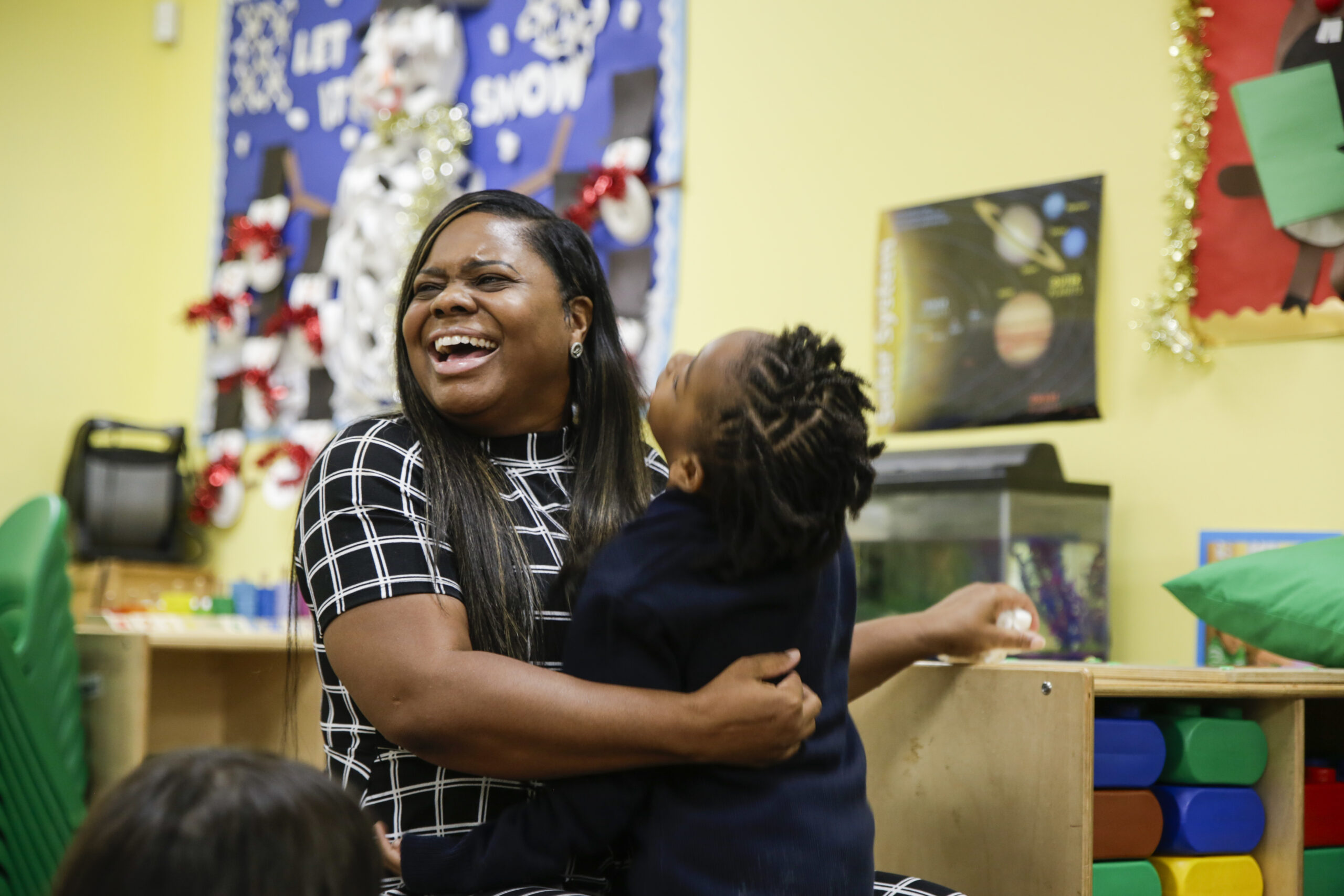 Tameki Warner, director of Learn Together Grow Together, sits smiling in a chair at story time with a child in her arms.