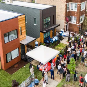 Aerial view of a community gathering near modern townhouses with a food truck and a tent set up, people are assembled in small groups outdoors.