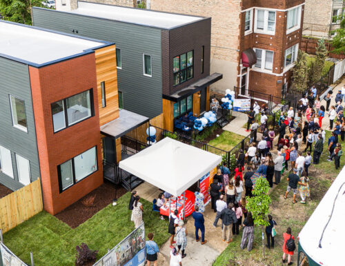 Aerial view of a community gathering near modern townhouses with a food truck and a tent set up, people are assembled in small groups outdoors.