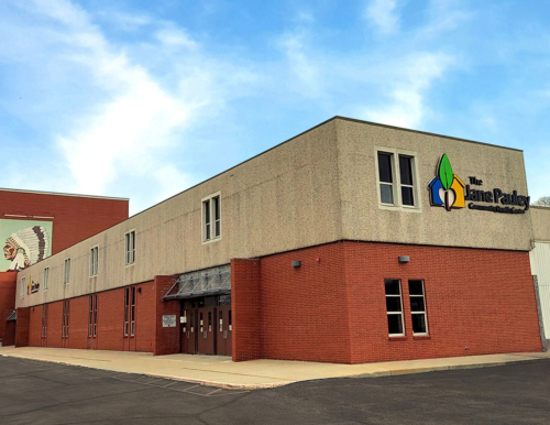 A building with beige and red brick facades, featuring the Jane Pauley Community Health Center logo on the right. A mural of a Native American headdress is on the adjacent red brick wall.