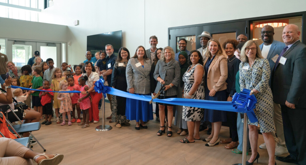 A group of people, including adults and children, standing at a ribbon-cutting ceremony with a bright blue ribbon.
