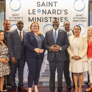 A diverse group of thirteen people posing in front of a "Saint Leonard's Ministries" banner.