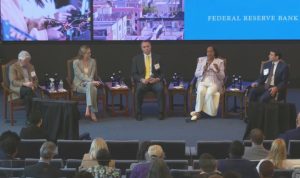 Panel discussion at a conference with five speakers seated on stage and an audience in front.