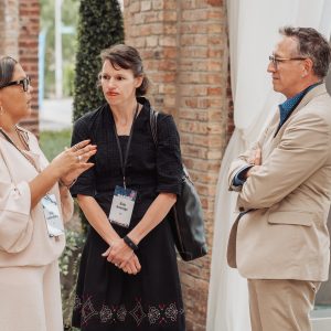 Three people stand in front of a brick pillar outside