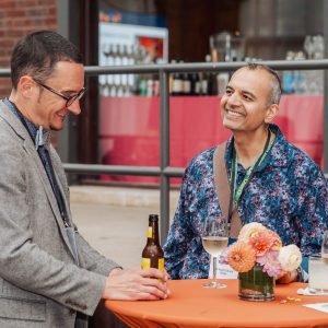 Two people stand at a small cocktail table and smile while talking