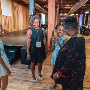 Two women stand with two young girls dressed in blue dancing outfits, in front of a stage