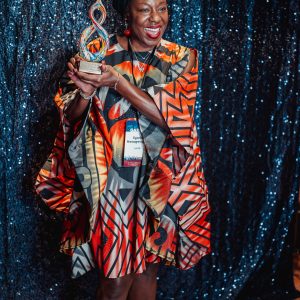 A woman poses in front of a sequin background while someone is taking her photo