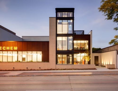 A modern building with large glass windows and "SHECHEM" sign illuminated in yellow.