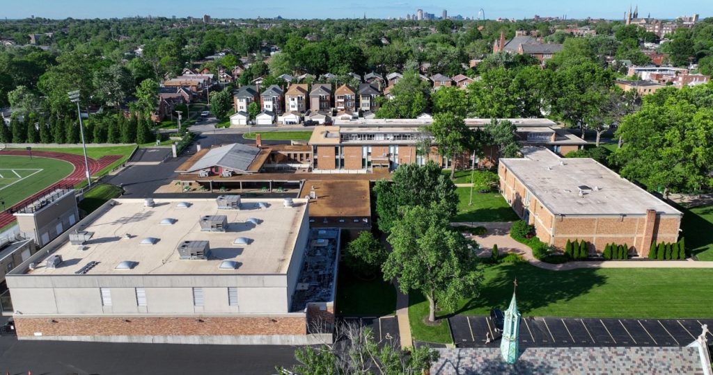 Aerial view of a school campus in a suburban area with houses and a distant city skyline.