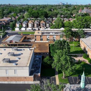 Aerial view of a school campus in a suburban area with houses and a distant city skyline.