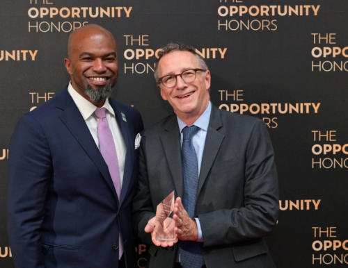 Two men in suits standing together, one holding an award, against a backdrop reading "THE OPPORTUNITY HONORS."