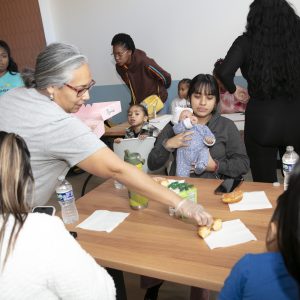 A group of people at a table, with a woman serving food and another holding a baby.