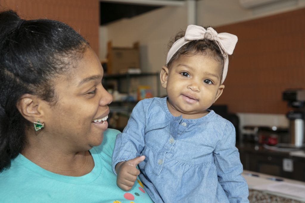 A woman smiling at an infant she is holding, both indoors.