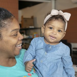 A woman smiling at an infant she is holding, both indoors.