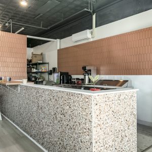 A modern café interior with a terrazzo counter and tan tiled wall.