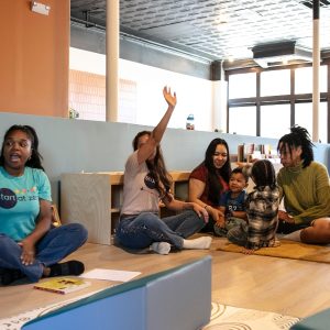 A group of adults and children interacting in an educational indoor setting with a woman holding a book.