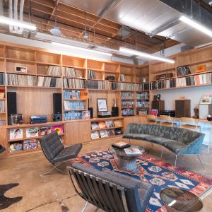 Interior of a wood-paneled room, with soft sofas and chairs, and shelves full of vinyl records and CDs, speakers, and record players