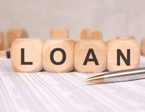 Wooden blocks spelling "LOAN" on a financial document with a pen and binder clip.