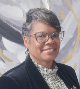 Portrait of a person with short gray hair and glasses, against an abstract background.
