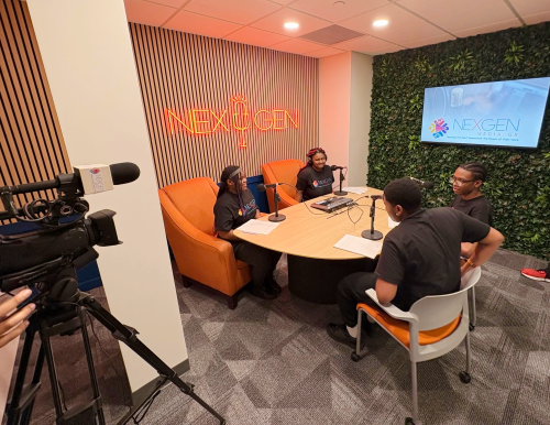 A group of young people engaged in a discussion around a table with microphones.