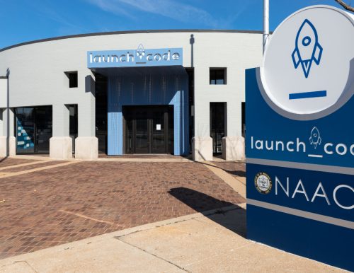 Exterior view of the LaunchCode building, featuring a rounded design, blue signage, and a brick walkway.